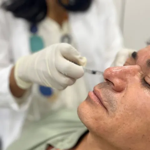 Profesional con guantes aplicando una inyección en el rostro de un paciente